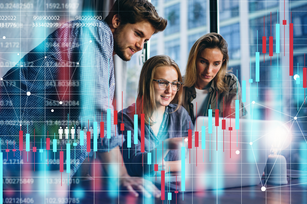 Three professionals collaborate over a laptop, surrounded by floating stock charts and data visuals in a modern office.