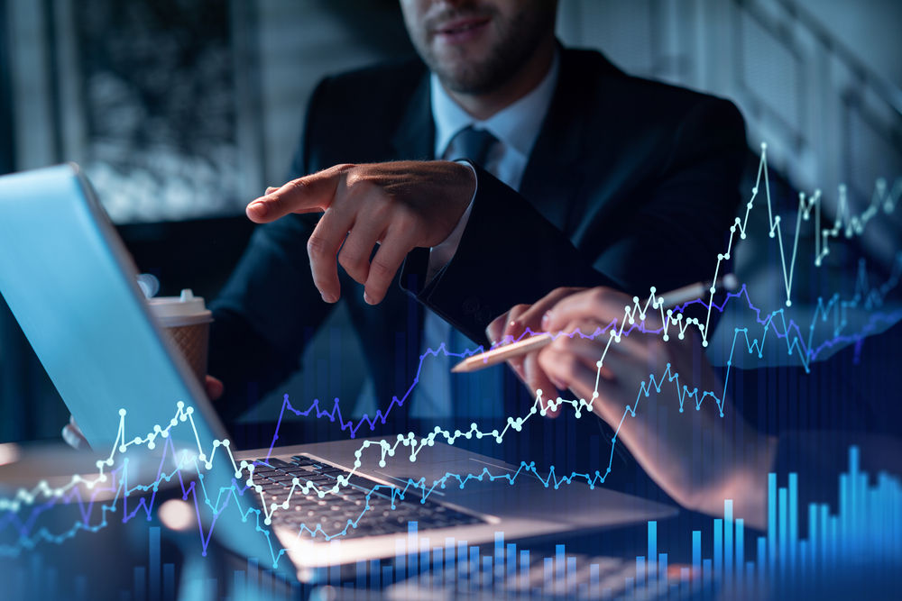 Businessperson points at a laptop screen with glowing stock charts and data lines.